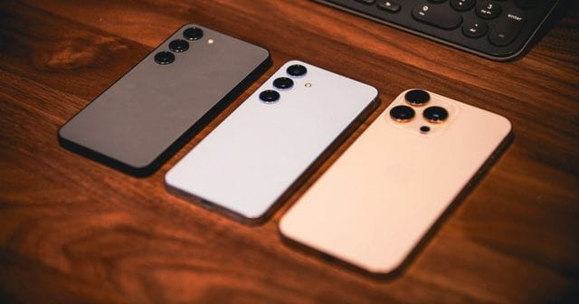 Tre smartphone recenti visti da dietro, uno accanto all'altro su un tavolo di legno