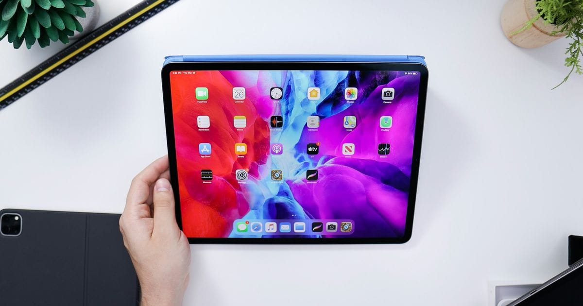 Una mano tiene un iPad Pro con la schermata Home accesa sopra una scrivania bianca