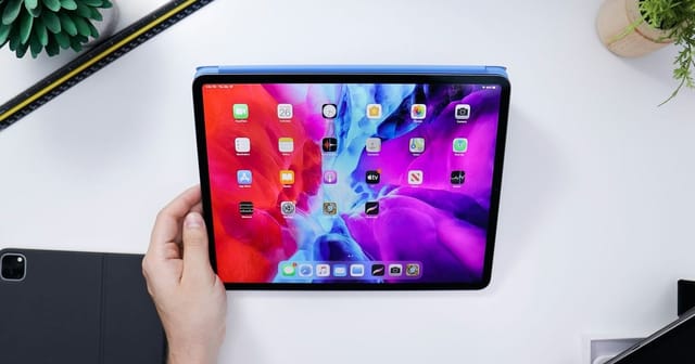 Una mano tiene un iPad Pro con la schermata Home accesa sopra una scrivania bianca