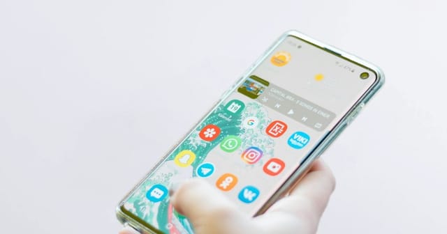 Una mano tiene uno smartphone Android in una cover trasparente, con la schermata Home accesa, su fondo bianco