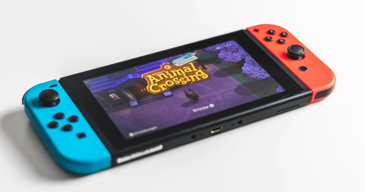 Nintendo Switch con Joy-Con blu e rosso su un piano bianco, sullo schermo Animal Crossing