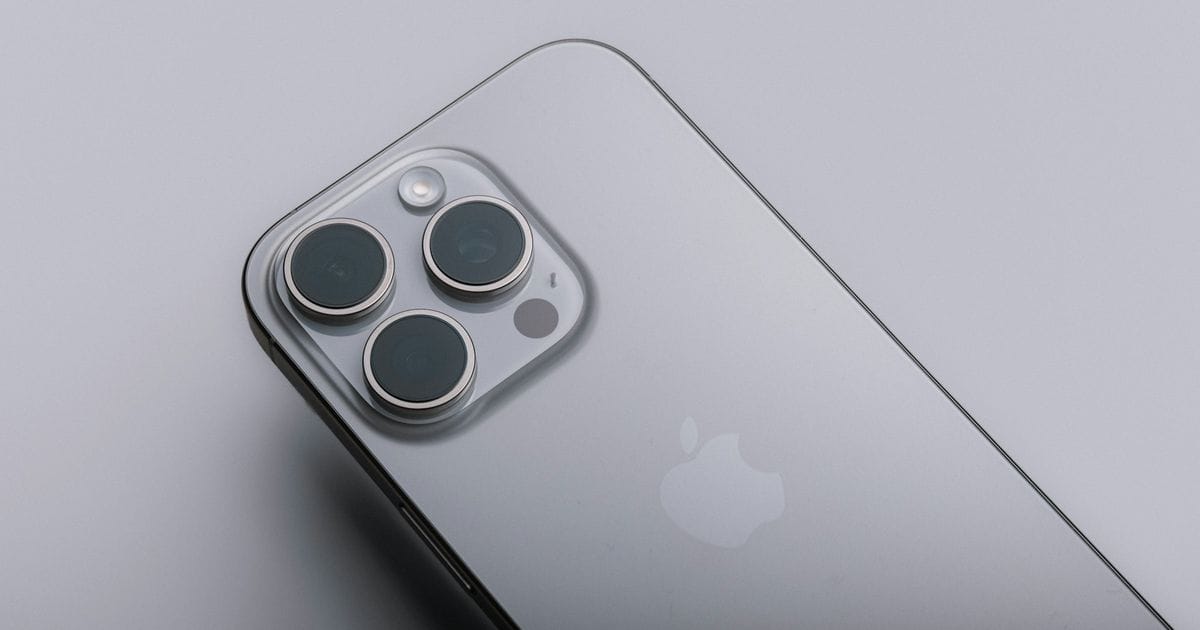 Primo piano del retro di un iPhone Pro grigio con la tripla fotocamera, su fondo grigio chiaro