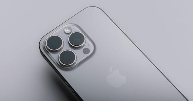 Primo piano del retro di un iPhone Pro grigio con la tripla fotocamera, su fondo grigio chiaro