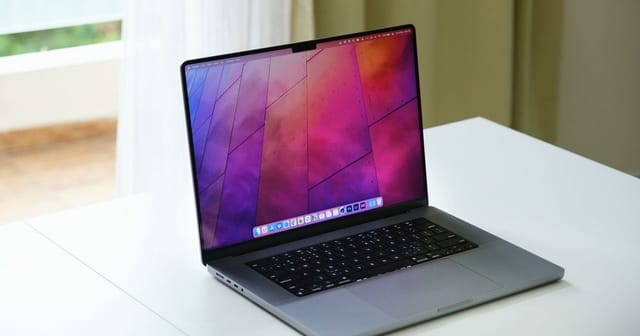 MacBook Pro aperto su un tavolo bianco accanto a una finestra luminosa