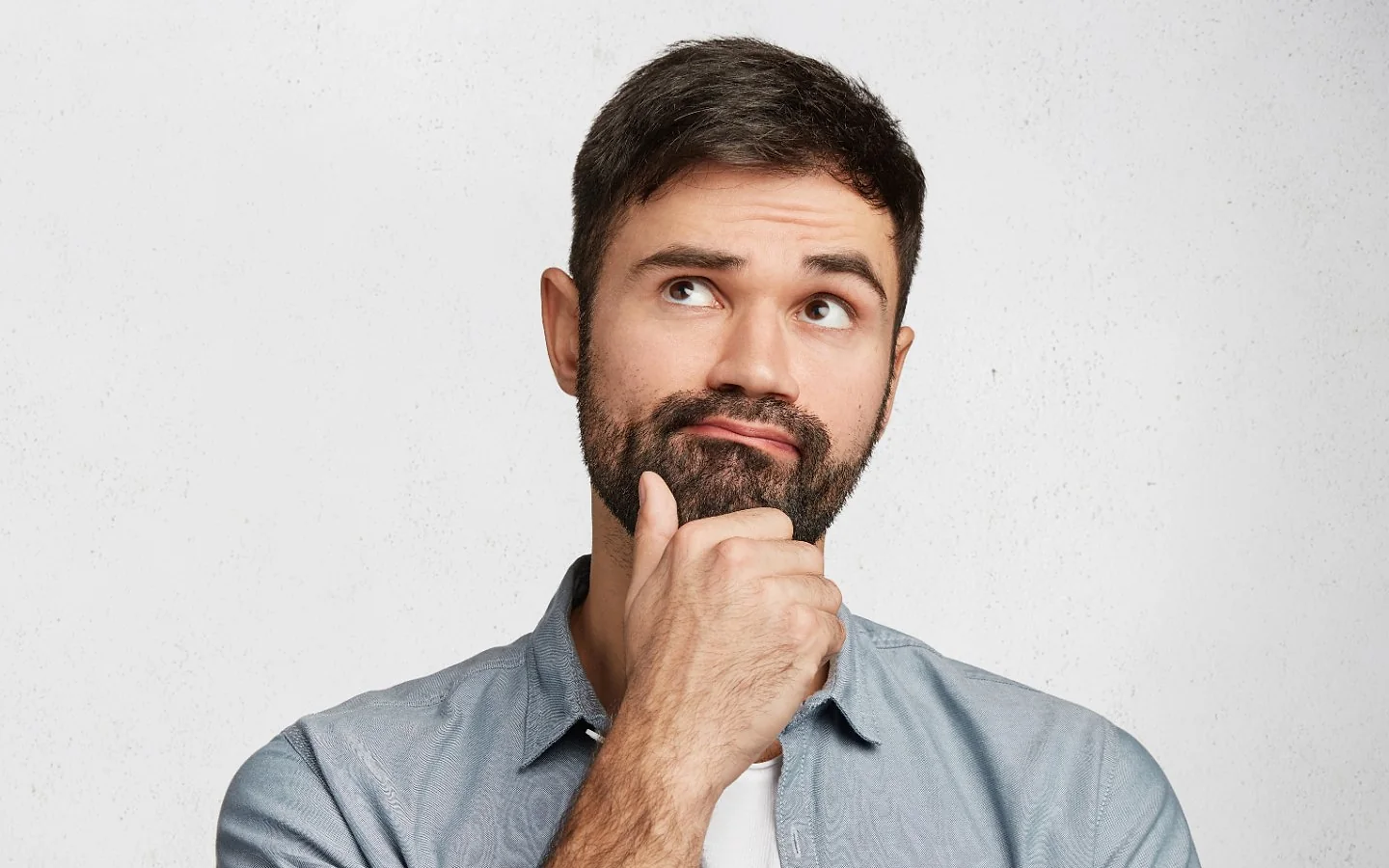 Un uomo con la barba, la mano sul mento, guarda in alto pensieroso
